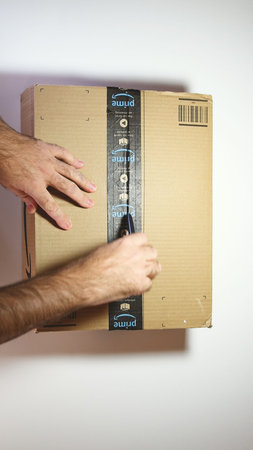 Paris, France - Feb 20, 2019: View from above of man hands unpacking new Amazon Prime cardboard box...