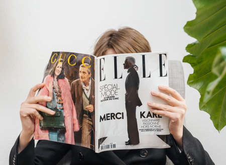 Paris, France - Feb 23, 2019: Woman reading French Elle magazine covering Karl Lagerfeld death, iconic fashion designer died aged 85 and was creative director at Chanel Fendi fashion housesのeditorial素材