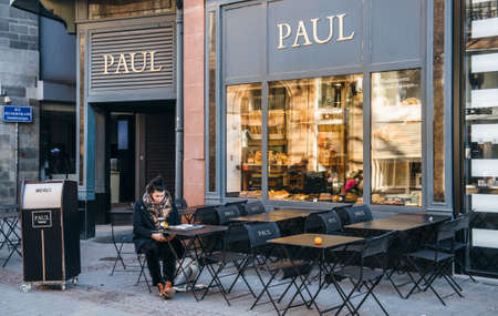 Strasbourg, France - Feb 16, 2018: Lonely woman eating croissant and drinking coffee at Paul cafe bakery terrace early in the morning in French cityのeditorial素材