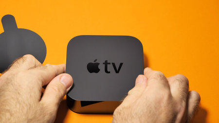 Paris, France - Oct 24; 2018: Male hands unboxing Apple TV against orange background - tv streaming device with apple logo on the topのeditorial素材