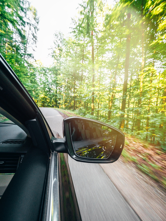 Vertical image of new modern car driving fast into forest with tall trees and empty mountain highway escaping running evading from all concept conceptの写真素材