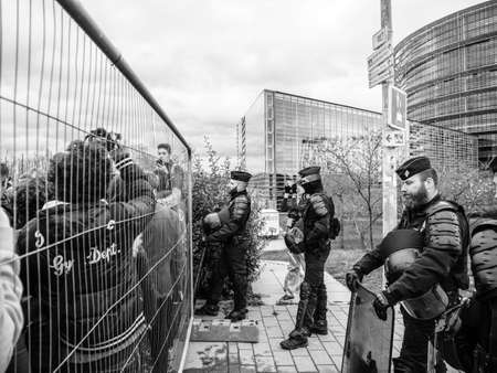 STRASBOURG, FRANCE - MAR 15, 2019: Police securing through fence from protesters near European Parliament during demonstrations against climate change global movement black and whiteのeditorial素材