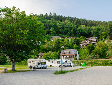 Schiltach, Germany - Jul 10, 2018: Couple resting in Chaise longue chairs in front of multiple RV camping recreational camping vehicles vans parked on the open air parking in the heart of black forest mountains in schiltach villageのeditorial素材