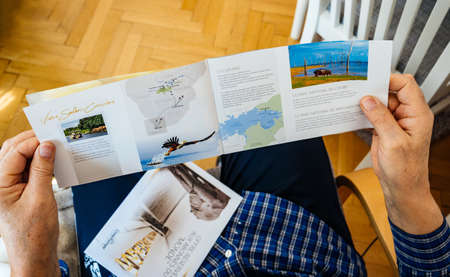 Paris, France - Mar 30, 2019: View from above of senior man holding reading new advertising leaflet from CroisiEurope an international river cruise company to South Africaのeditorial素材