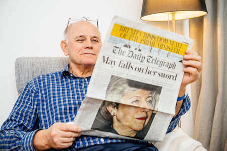 Paris, France - 29 Mar 2019: Smiling senior man reading in living room latest british The Daily Telegraph newspaper UK press featuring Theresa may PM on front coverのeditorial素材