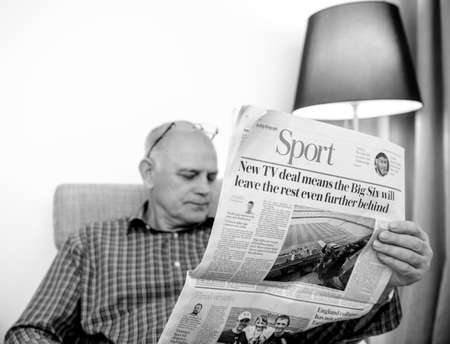 Paris, France - 29 Mar 2019: Senior man reading in living room latest british The Daily Telegraph newspaper UK press Sport section of the newspaper black and whiteのeditorial素材