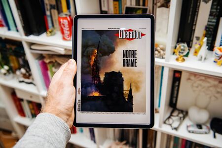 Paris, France - Apr 15, 2019: Man reading on iPad Pro Apple News Plus digital newspaper featuring on cover Notre-Dame Cathedral on fire causing damages the famous spire to collapse Liberation Notre-Drameのeditorial素材