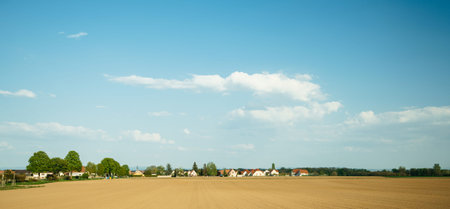 Typical French village with multiple houses, church, large area of plowed fields and clear blue sky...