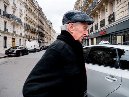 Paris, France - Jan 1, 2018: senior man walking in front of the camera near taxi car on the Rue de Maubeuge near Gare de Nord train station with Monoprix supermarket in backgroundのeditorial素材