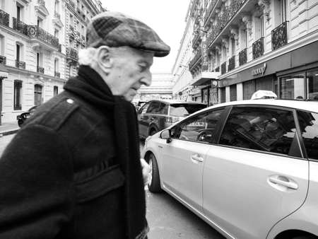 Paris, France - Jan 1, 2018:  senior man walking in front of the camera near taxi car on the Rue de Maubeuge near Gare de Nord train station with Monoprix supermarket black and whiteのeditorial素材