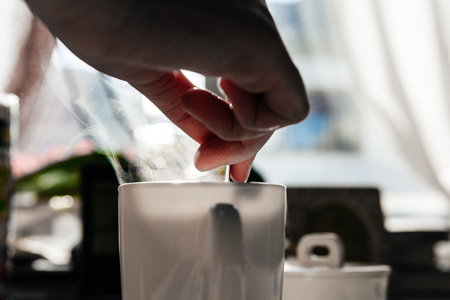Woman holding teaspoon inside white coffee mug with tiny particles of the steam vaporの写真素材