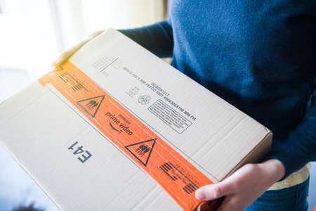 Paris, France - MAr 16, 2019: Woman with Amazon Prime Video logotype on the cardboard box carton parcel with red security sealing tape membership streaming service and Prime Original The Grand Tourのeditorial素材