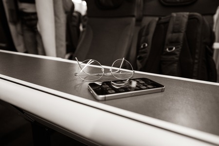 Focus on titanium eyewear glasses with new modern smartphone on train table inside British train black and whiteの写真素材