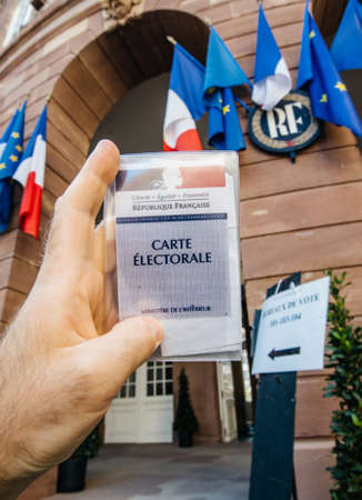 Strasbourg, France - May 26, 2019: Vertical image of man hand holding Voters car French Carte Electorale with entrance to Hotel de Ville city hall on the 2019 European Parliament election dayのeditorial素材