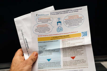 Paris, France - Apr 9, 2019: Man reading holding la declaration des revenus income statement instruction before submitting pre-filled income statement to French authorities and income tax instruction for previous yearのeditorial素材