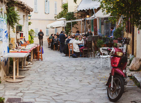 Athens, Greece - Mar 28, 2016: Tiny cute Greek street with people enjoying food on the terrace cafe in cozy vintage neighborhoodのeditorial素材