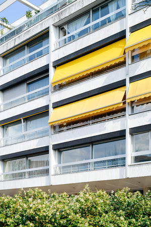 French 70s architectural style building with yellow awnings on balconies opened - covered by sun-shield on a warm summer dayの写真素材