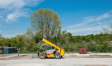 Yellow modern new forklift in empty construction site under clear blue sky