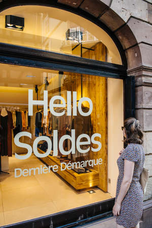 Strasbourg, France- Jul 22, 2017: Young woman in front of large showcase window with Hello Soldes Derniere Demarque Hello sales last call for best price for clothes fashion storeのeditorial素材