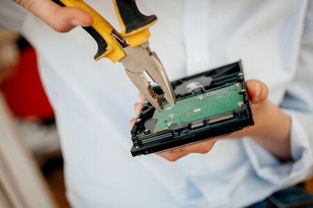 Female IT computer repair IT woman using yellow metal pliers to fix broken poor manufacture HDD disk drive with valuable stored data information open green boardの写真素材
