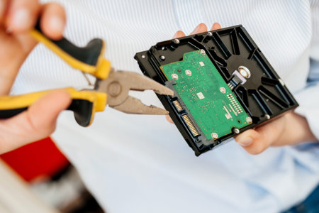 Hands IT computer repair engineer using yellow metal pliers to fix broken poor manufacture HDD disk...