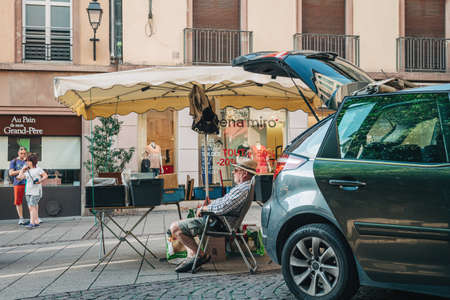 Strasbourg, France - July 22, 2017: Senior man with hat sitting in chair relaxed waiting for customers to buy used books at daily flea market in central Strasbourgのeditorial素材