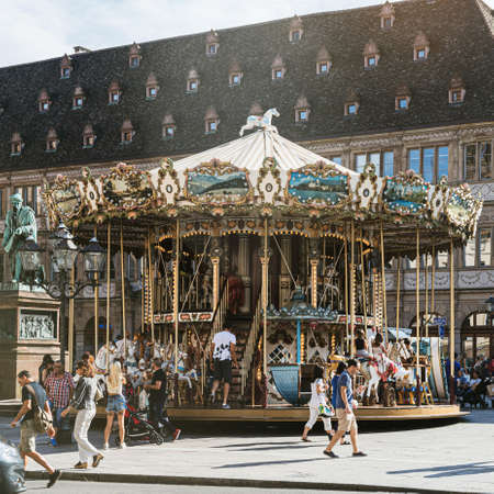 Strasbourg, France - July 22, 2017: Square image of large group of people having fun at the merry-go-round carousel in Place Gutenberg, Alsace on a warm summer dayのeditorial素材