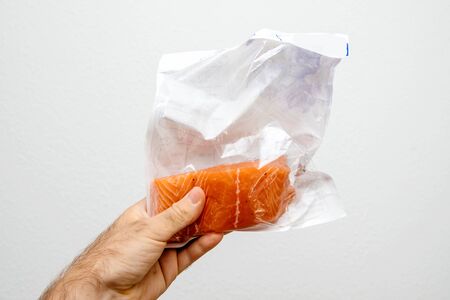 Man hand holding against white background plastic sealed package with fresh salmon steakの写真素材