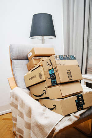 Paris, France - Jun 4, 2019: Stack of multiple cartoon cardboard boxes with Amazon Prime smile icon on the Ikea chair in living room - overflow by ecommerce shoppingのeditorial素材