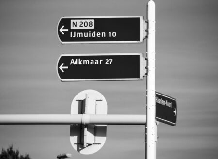 Futch street highway sign with directions to IJmuiden, Alkmaar,- clear sky inthe background - black and whiteの写真素材