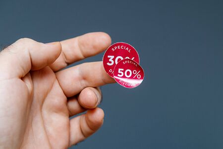 Man hand with glue sticked discount sale special price 30 than 50 percent red tags to be glued on goods during sale season - isolated gray background