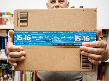 PARIS, FRANCE - JUL 12, 2108: Senior man holding Amazon Prime Day cardboard parcel with special blue scotch tape for the Prime Day offering a day of deals, discounts, and unabashed shoppingのeditorial素材