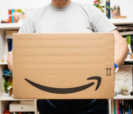 PARIS, FRANCE - JUL 12, 2108: Senior man holding Amazon Prime cardboard parcel with special blue scotch tape for the Prime Day offering a day of deals, discounts, and unabashed shoppingのeditorial素材