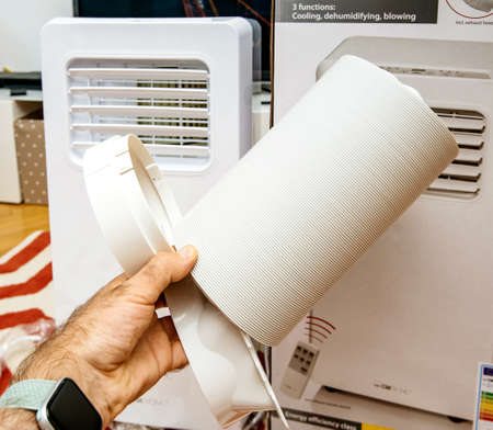 Paris, France - Jun 23, 2019: Young man unboxing installing new portable air conditioner unit AC during hot summer in his living room inspecting the supplied accessoriesのeditorial素材