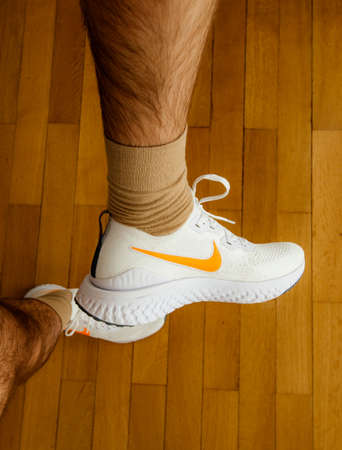 Paris France - Jul 13 2019: Man measuring new Nike Epic React Flyknit 2 running shoes equipment on the living room wooden floor manufactured by Nike sportswear showing white icon on side of the shoeのeditorial素材