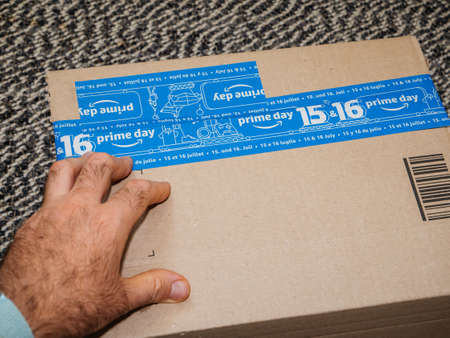 PARIS, FRANCE - JUL 4 2109: Man hand preparing to unbox unpacking new Amazon Prime Day cardboard parcel with special blue tape for the Prime Dayのeditorial素材