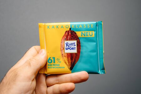 Paris, France - Apr 27, 2019: Man hand holding delicious Ritter Sport Cacao Classe with 61 percent chocolate against gray backgroundのeditorial素材