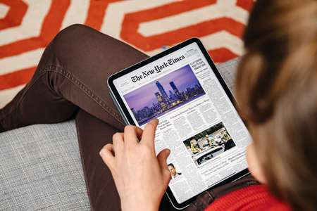 Paris, France - Mar 15, 2019: Woman reading on digital iPad Pro tablet the latest newspaper The New York Times cover with breaking news about Manhattan business districtのeditorial素材