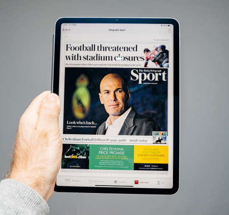 Paris, France - Mar 15, 2019: Man reading on digital iPad Pro tablet the latest The Daily Telegraph Sport newspaper cover with breaking news about Zinedine Zidaneのeditorial素材