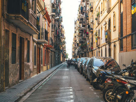 Barcelona, Spain - Bov 15, 2017: Pedestrians walking between tall Spanish architecture apartment buildings on a tiny street in central barcelona with parked popedes and carsのeditorial素材