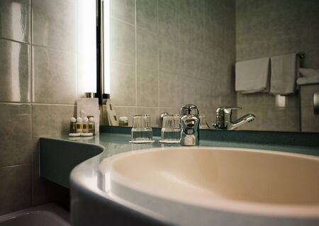 Interior of modern three star hotel with sink, chrome water tap, two glasses and defocused shampoo in the cornerの写真素材