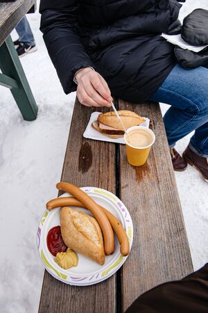 Woman eating traditional German wurst sausage and traditional meat drinking a hot coffee while visiting the snow mountain resortの写真素材