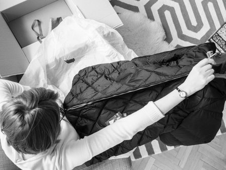 Overhead view of elegant fashionable woman unboxing new luxury winter parka from the delivered...