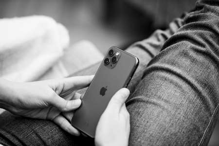 Paris, France - Sep 27, 2019: Black and white image of Elegant young woman looking at matte glass of latest Apple Computers iPhone 11 Pro with triple-camera using smartphone in business living room sofaのeditorial素材