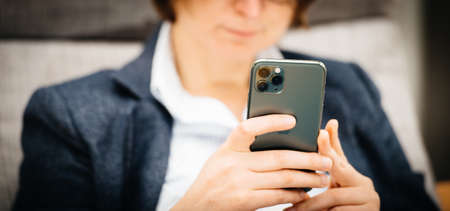 Paris, France - Sep 27, 2019: Front view of elegant young woman holding latest Apple Computers iPhone 11 Pro with triple-camera using smartphone in business living room sofaのeditorial素材
