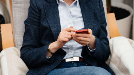 Paris, France - Sep 27, 2019: Woman using old Apple iPhone SE mobile phone in red leather case in cosy office chairのeditorial素材