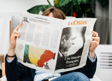Paris, France - Sep 27, 2019: Woman reading La Croix in living room newspaper following the death of...