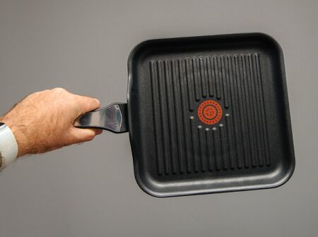 Man hand holding new grill pan isolated on gray backgroundの写真素材