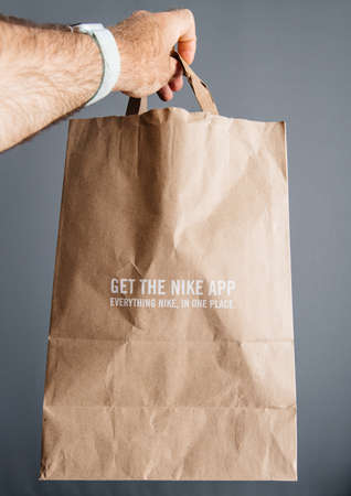 Paris, France - Sep 30. 2019: Male hand holding new Nike Plus paper bag with new sports equipment bought from a Nike Store - get the Nike App everything in one placeのeditorial素材