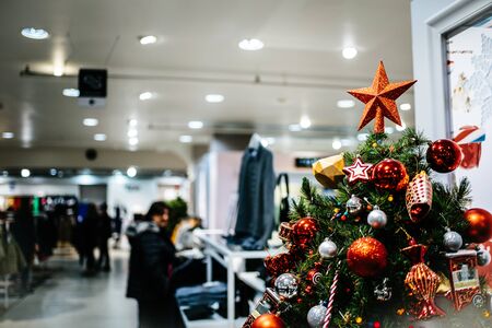 Detail of elegant Christmas tree decorated with red glass ornaments inside large supermarkt fashion mall during winter holidays with people customers shopping in backgroundの写真素材